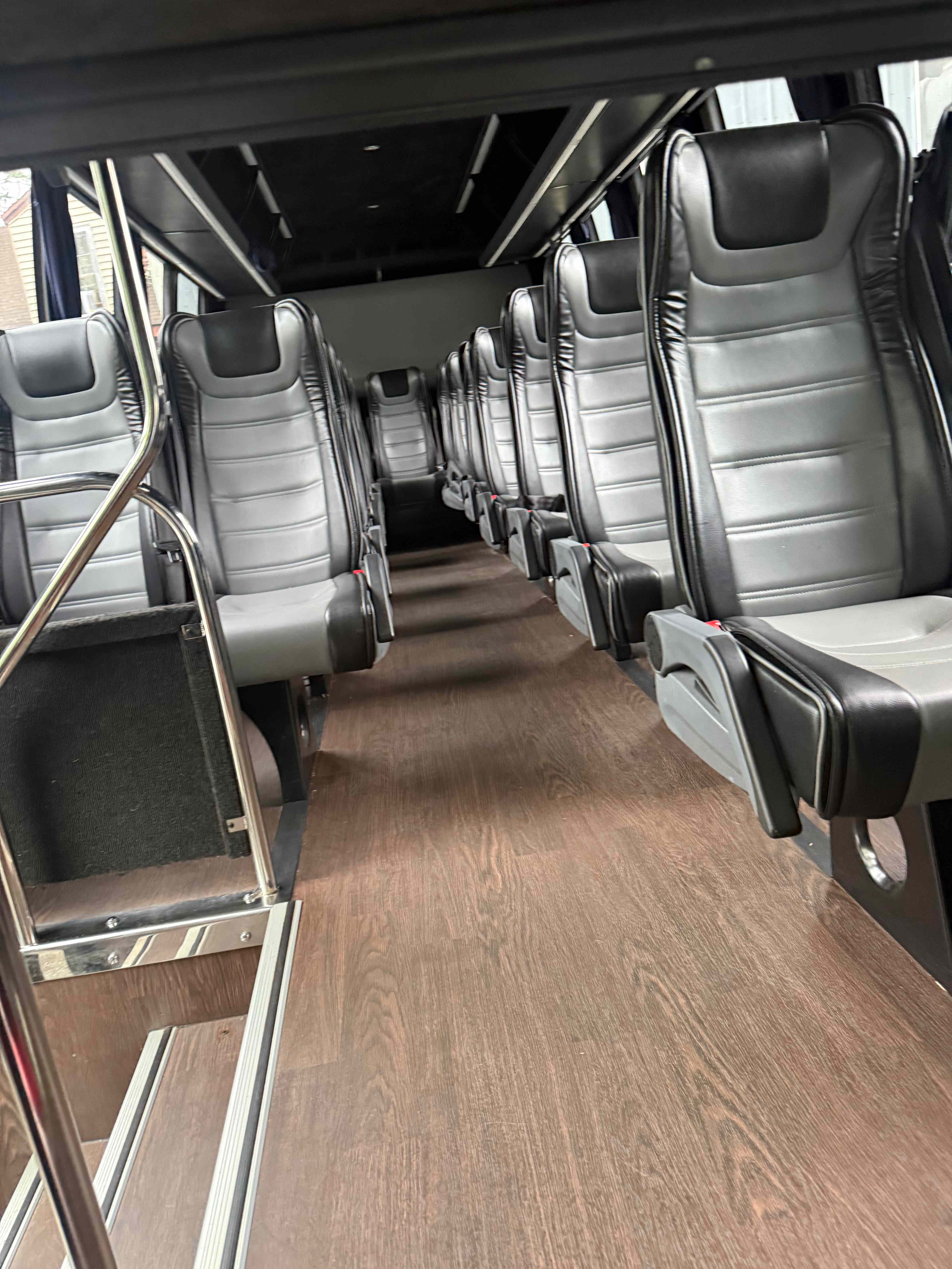 Mini coach bus interior aisle view with reclining leather seats and wood-style flooring